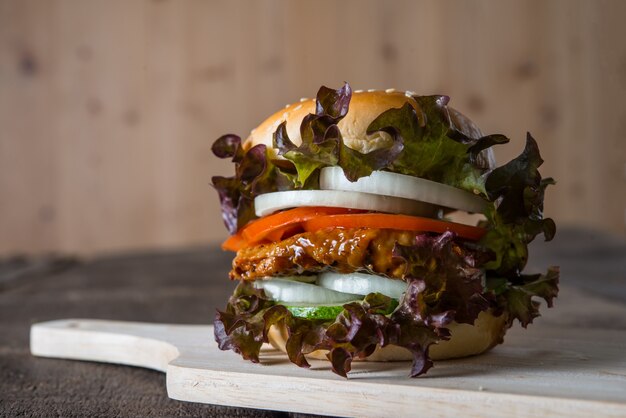 Hamburger di pollo fatto in casa con lattuga, pomodoro e cipolla sulla tavola di legno.