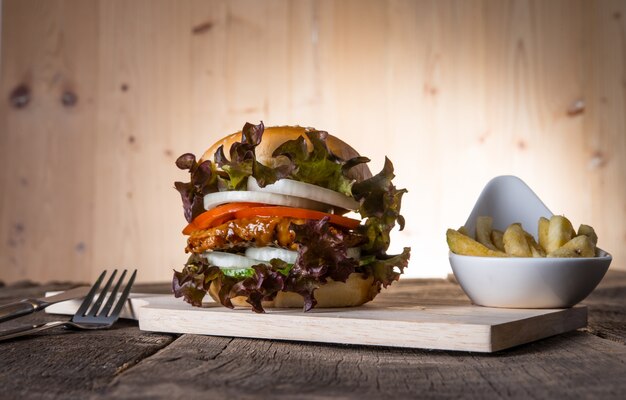 Hamburger di pollo fatto in casa con patatine fritte, lattuga, pomodoro e cipolla sulla tavola di legno.