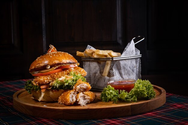 Hamburger di pollo succoso con lattuga fresca e patatine fritte croccanti su una tavola di legno