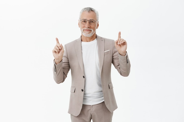 Handsome imprenditore sorridente in bicchieri e tuta puntando le dita verso l'alto, mostrando pubblicità