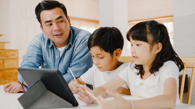 Happy Asia family homeschooling, padre insegna ai bambini utilizzando il tablet digitale nel soggiorno di casa.