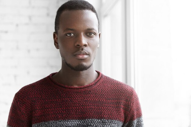 Headshot di bel giovane maschio africano con la barba lunga che indossa un maglione accogliente casual