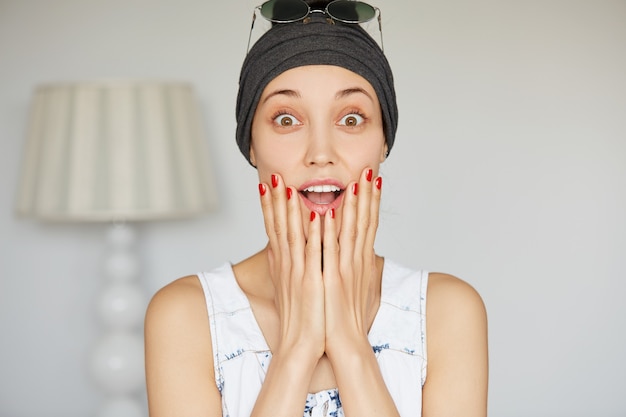 Headshot isolato della ragazza dell'allievo che guarda sorpresa con le mani sulle sue guance, bocca spalancata