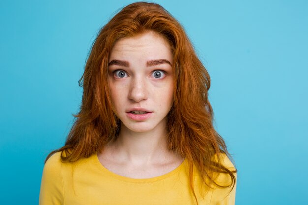 Headshot Ritratto di ragazza felice di capelli rossi zenzero con lentiggini sorridente guardando la fotocamera. Sfondo blu pastello. Copia spazio.
