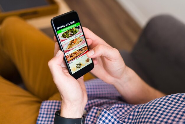 Ho fame. Mani di un uomo che guarda un'app per la consegna di cibo sul suo smartphone e ordina la cena online