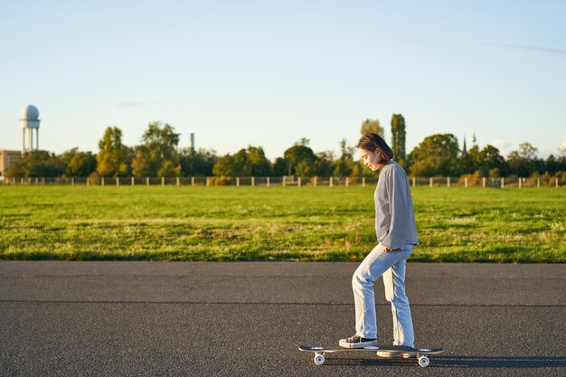 Hobby e stile di vita giovane donna che guida skateboard skater ragazza che si gode la crociera su longboard su sunn