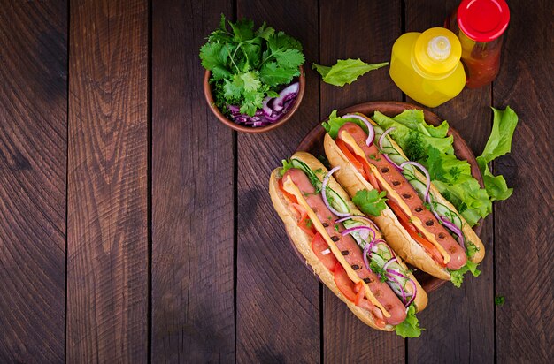 Hot dog con salsiccia, cetriolo, pomodoro e lattuga sul tavolo di legno scuro. Hot dog estivo. Vista dall'alto