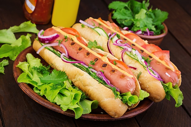 Hot dog con salsiccia, cetriolo, pomodoro e lattuga sul tavolo di legno scuro. Hot dog estivo.