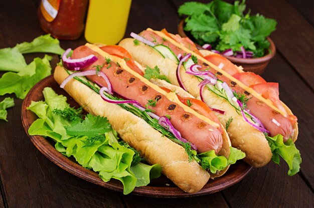 Hot dog con salsiccia, cetriolo, pomodoro e lattuga sul tavolo di legno scuro. Hot dog estivo.