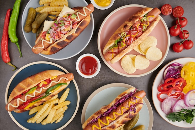 Hot dog di manzo alla griglia gourmet con lati e patatine. Deliziosi e semplici hot dog con senape, pepe, cipolla e nachos. Hot dog completamente caricati con condimenti assortiti su una tavola da paddle.