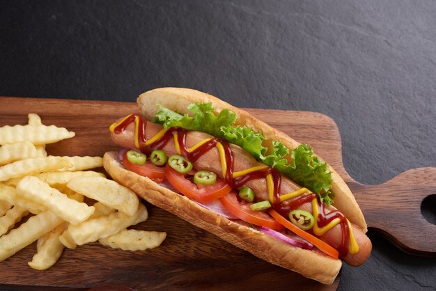 Hot dog di manzo alla griglia gourmet con lati e patatine. Deliziosi e semplici hot dog con senape, pepe, cipolla e nachos. Hot dog completamente caricati con condimenti assortiti su una tavola da paddle.