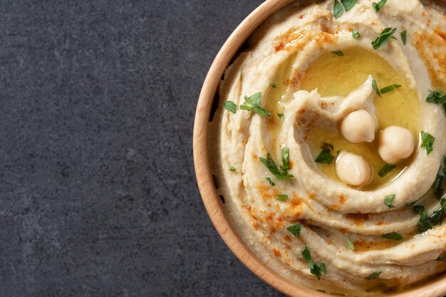 Hummus di ceci in una ciotola di legno guarnita con prezzemolo, paprika e olio d'oliva Primo piano