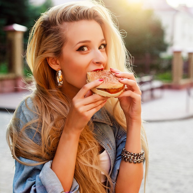 Hungry giovane donna di mangiare un gustoso hamburger