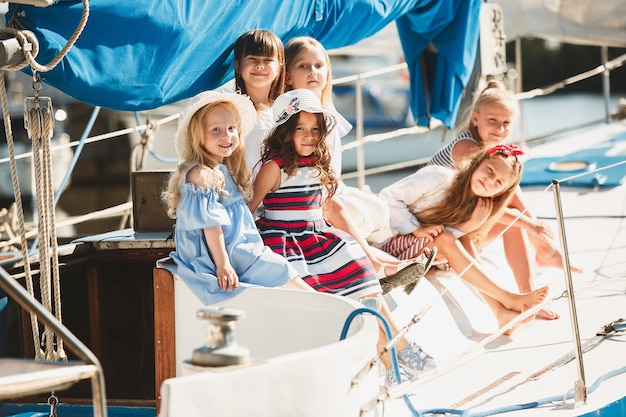 I bambini a bordo dello yacht del mare bevono succo d'arancia. Le ragazze adolescenti o bambini contro il cielo blu all'aperto. Vestiti colorati. Concetti di moda per bambini, estate soleggiata, fiume e vacanze.