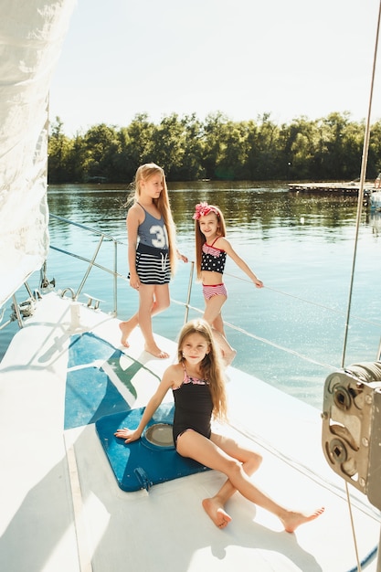 I bambini a bordo dello yacht del mare bevono succo d'arancia. Le ragazze adolescenti o bambini contro il cielo blu all'aperto. Vestiti colorati. Concetti di moda per bambini, estate soleggiata, fiume e vacanze.