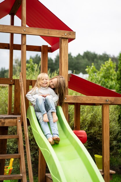 i bambini cavalcano dallo scivolo dei bambini, le sorelle giocano insieme nel giardino