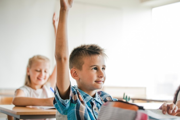 I bambini che si siedono ai banchi della scuola che sollevano le mani