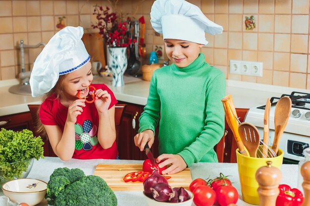 I bambini divertenti della famiglia felice stanno preparando un'insalata di verdure fresca nella cucina