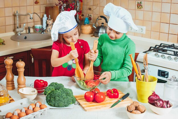 I bambini divertenti della famiglia felice stanno preparando un'insalata di verdure fresca nella cucina