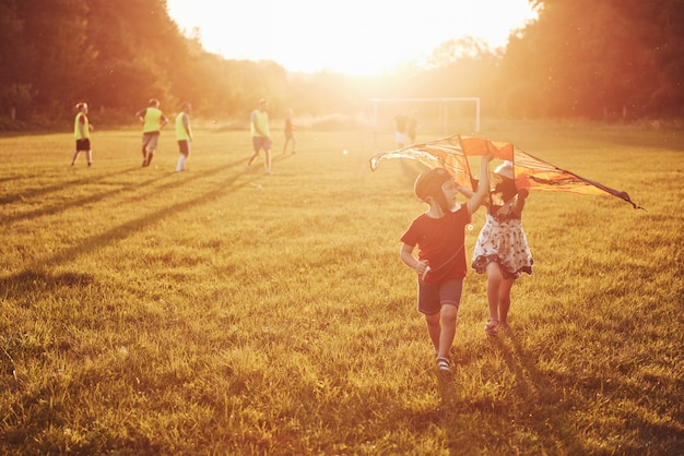 I bambini felici lanciano un aquilone nel campo al tramonto. Ragazzino e ragazza in vacanza estiva