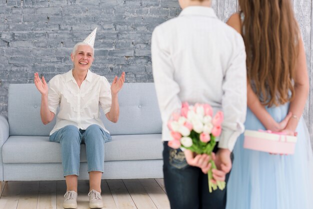 I bambini nascondono doni alle loro spalle in piedi di fronte alla loro nonna