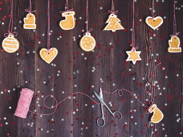 I biscotti del pan di zenzero su corda per la decorazione dell&#39;albero di Natale con le forbici e filano il nuovo anno sulla tavola di legno