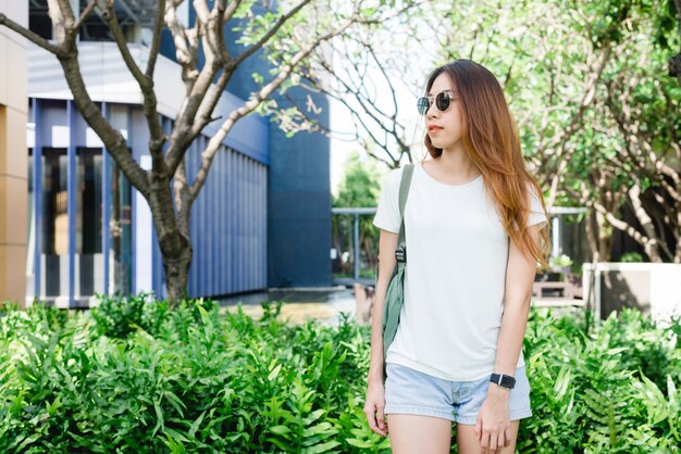I capelli marroni lunghi della ragazza asiatica dei pantaloni a vita bassa in maglietta in bianco bianca sta stando nel mezzo della via