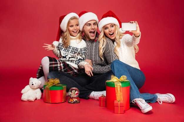 I cappelli da portare di natale della giovane famiglia felice sveglia fanno il selfie