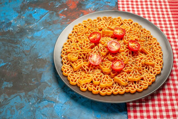 I cuori di pasta italiana di vista dal basso hanno tagliato i pomodorini sul piatto sul tavolo a quadretti bianco rosso