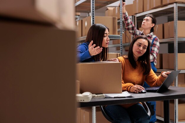 I dipendenti del magazzino controllano la soddisfazione della consegna del cliente sul laptop e discutono sul feedback negativo. Colleghe di donne asiatiche del servizio postale che gestiscono la spedizione dal computer del magazzino