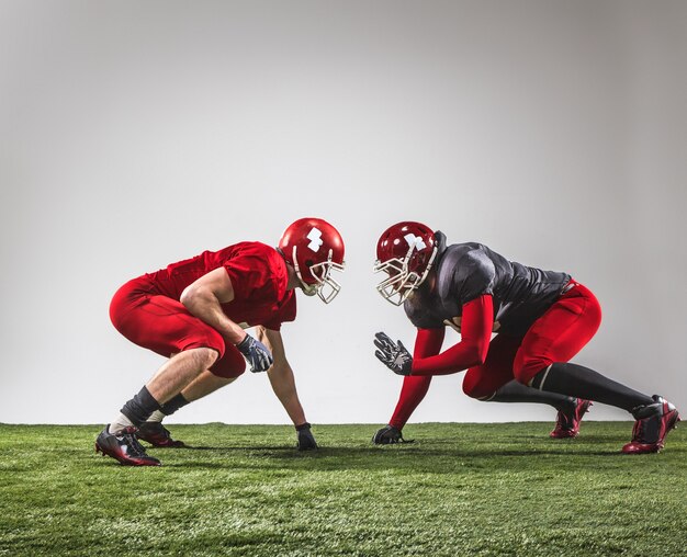 I due giocatori di football americano in azione su erba verde e sfondo grigio.