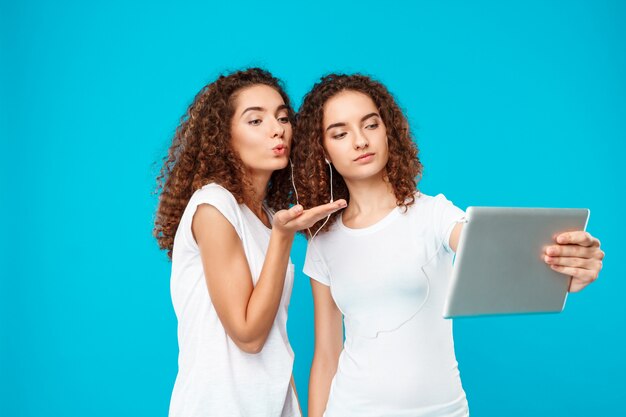 I gemelli di due womans che fanno selfie sulla compressa sopra il blu.