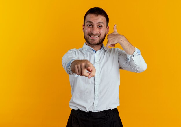 I gesti sorridenti dell'uomo bello mi chiamano segno della mano che indica isolato sulla parete arancione