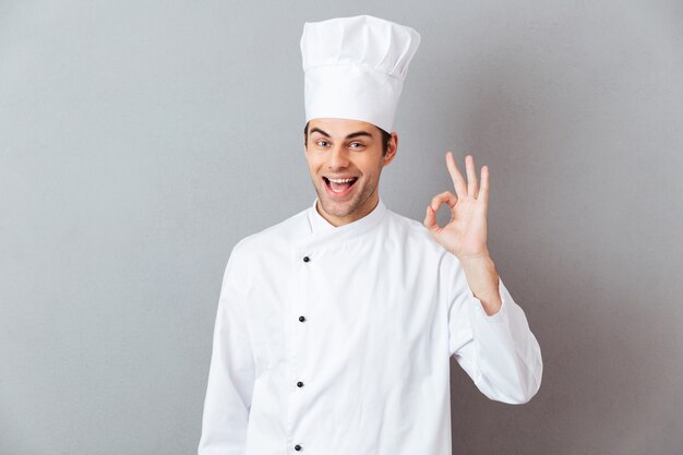 I giovani allegri cucinano in uniforme che mostra il gesto giusto.