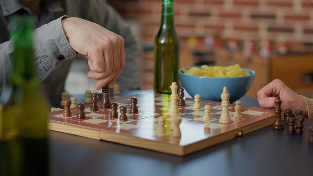 I giovani si divertono con i giochi da tavolo a scacchi, servendo bevande alcoliche e snack. Gruppo di amici che giocano a una partita sul tavolo per l'intrattenimento al raduno. Scatto da treppiede. Avvicinamento.