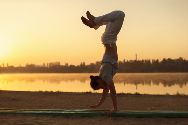 I giovani uomini atletici che stanno nell'yoga posano sul lago vicino nel parco