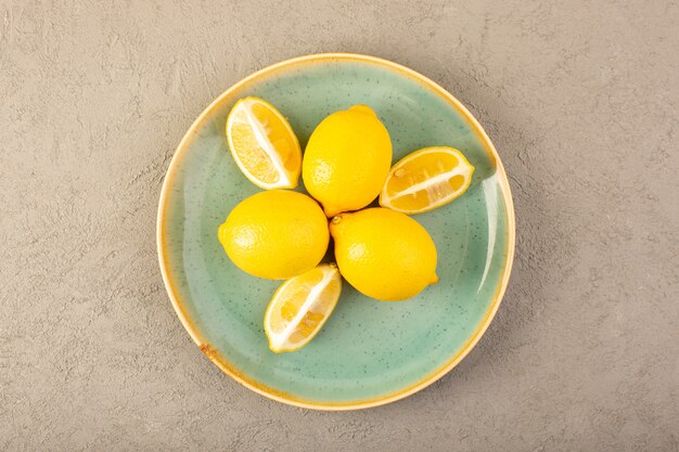 I limoni freschi gialli di una vista superiore maturano intero dolce e succoso e affettato dentro il piatto verde sul fondo grigio fruttifica colore dell'agrume