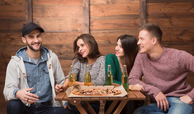 I migliori amici che riposano in pizzeria e grandi sorridenti eccitati. Tre amici che guardano il loro amico felice in berretto e aspettano la sua reazione.