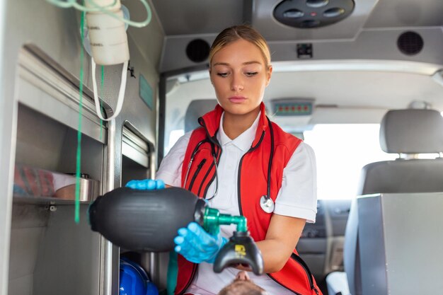 I paramedici EMS forniscono assistenza medica a un paziente ferito in viaggio verso un assistente ospedaliero per le emergenze indossando una maschera di ventilazione con rianimatori manuali in silicone in un'ambulanza