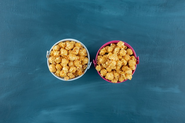 I piccoli secchi hanno riempito l'orlo di popcorn al caramello su sfondo blu. Foto di alta qualità