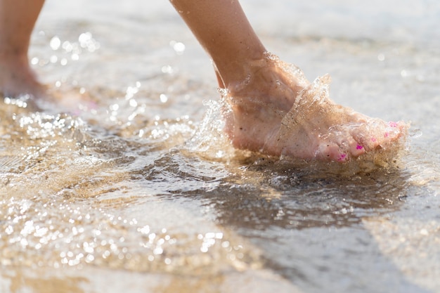 I piedi delle donne attraverso la sabbia della spiaggia e l'acqua