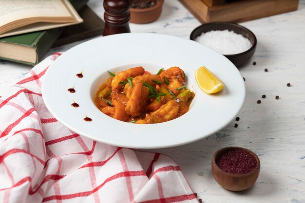 I piedi di pollo in umido in salsa di pomodoro in una ciotola bianca con verdure e limone.