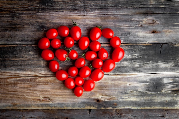 I pomodori di vista superiore che formano il cuore modellano su fondo di legno scuro. spazio orizzontale per il testo