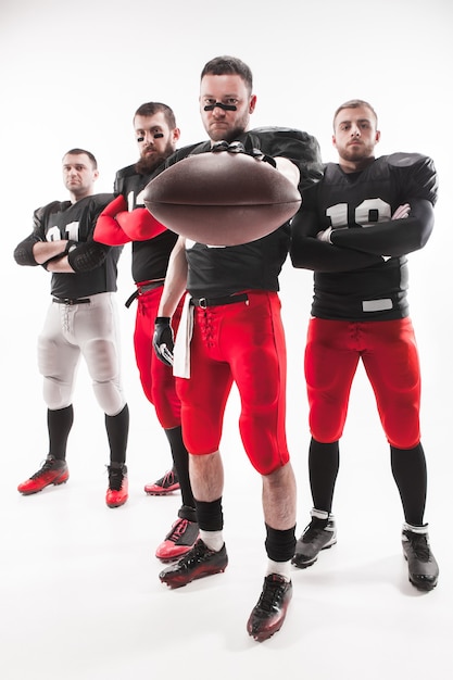 I quattro uomini caucasici di fitness come giocatori di football americano in posa a figura intera con una palla su sfondo bianco