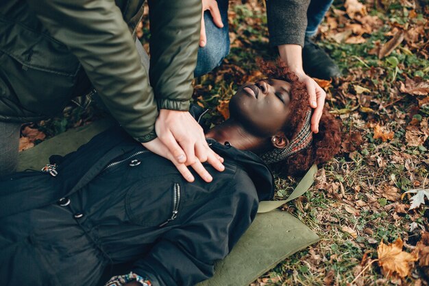 I ragazzi aiutano una donna. La ragazza africana sta mentendo inconscia. Fornire il primo soccorso nel parco.