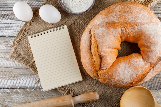 Il bagel ha tagliato a metà con il blocco note, le uova, il matterello sul panno di sacco e la superficie di legno, vista superiore.