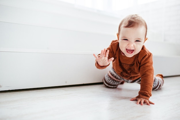 Il bambino felice in maglione arancione gioca con la piuma sul pavimento