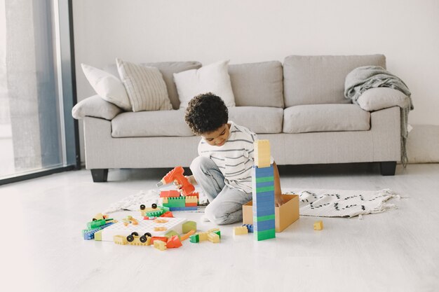 Il bambino gioca con i giochi sul pavimento. Il bambino africano compone un costruttore. Capelli ricci in un ragazzo.
