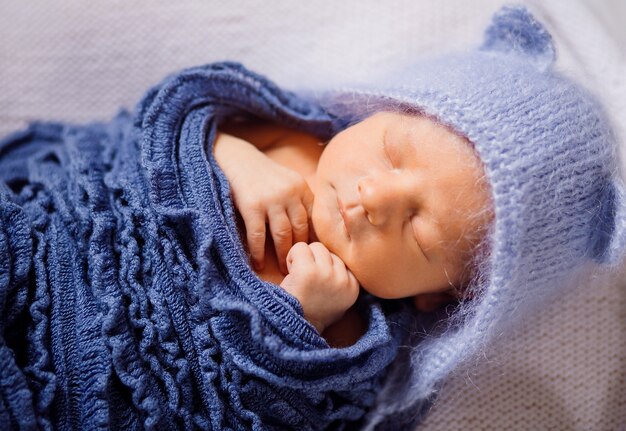 Il bambino in cappello blu e sciarpa lavorata a maglia dorme sul cuscino bianco