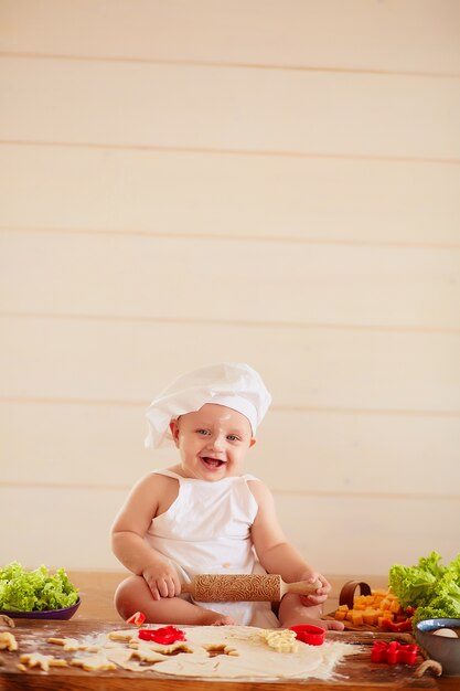 Il bambino piccolo si siede sul tavolo vicino a pasta e verdure